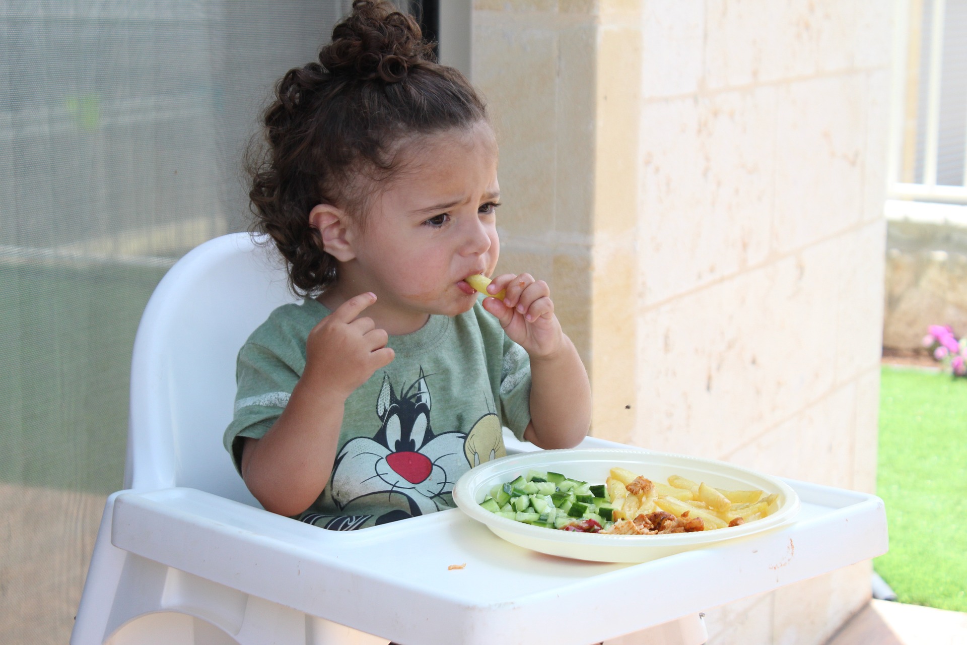 A young girl eats a french fry while sitting in her high chair
