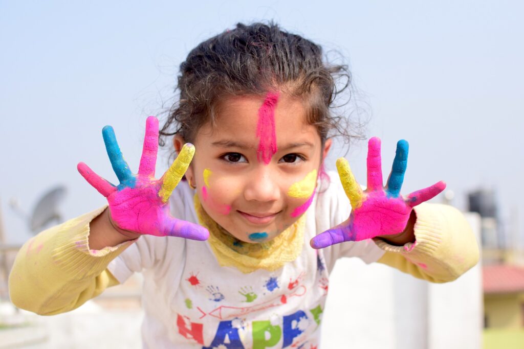 A girl shows her two hands completely covered in colorful paint