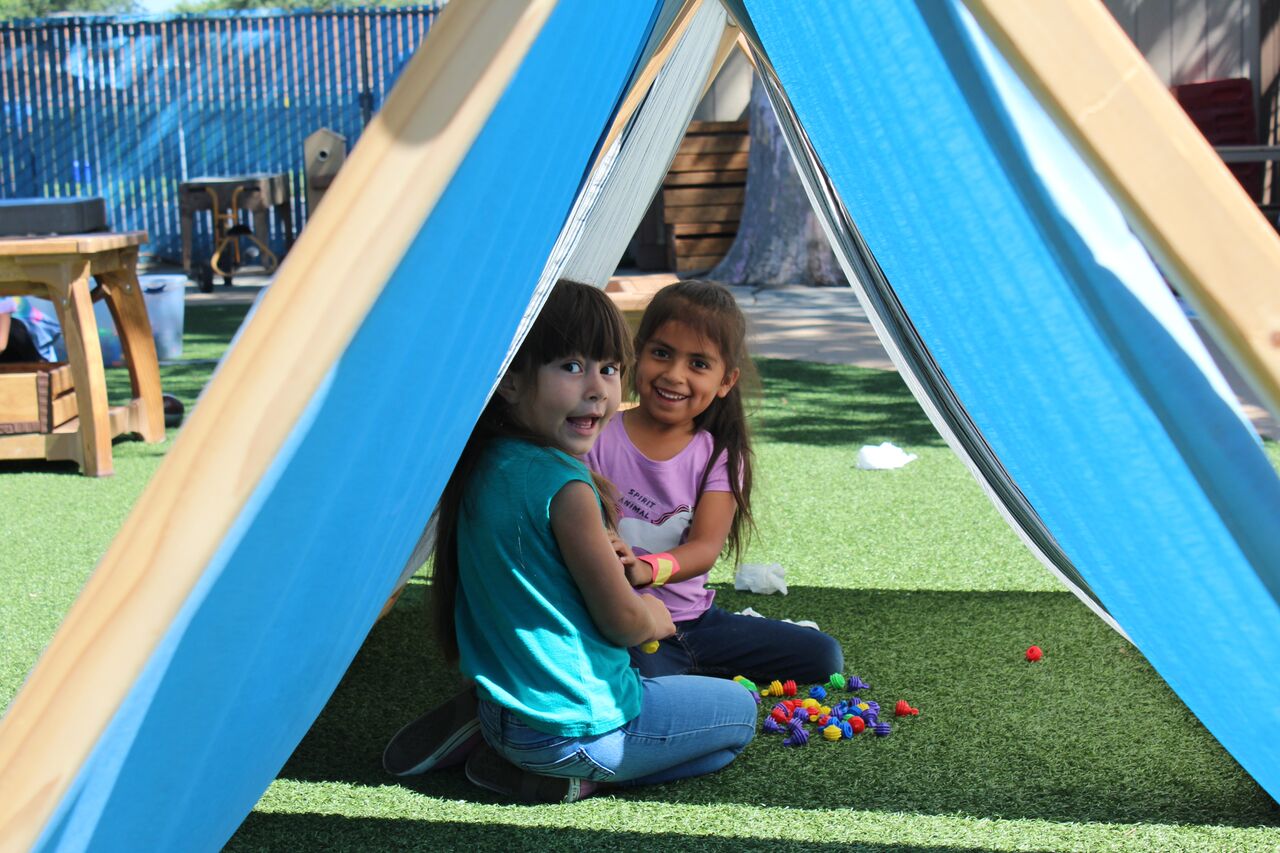 Two young girls playing in a tent outside