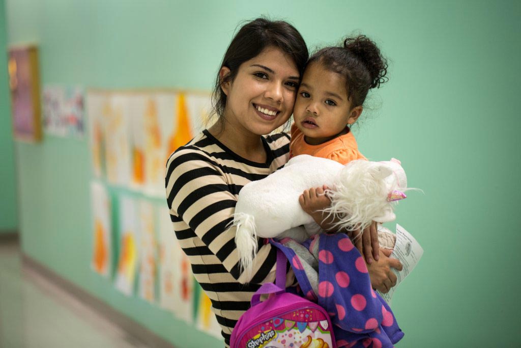 A child care worker holding a young child and smiling for the camera