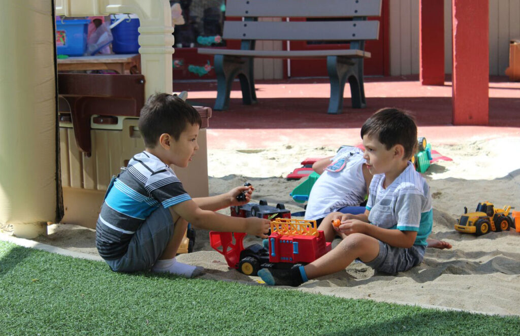 Two young boys play together in a sand box